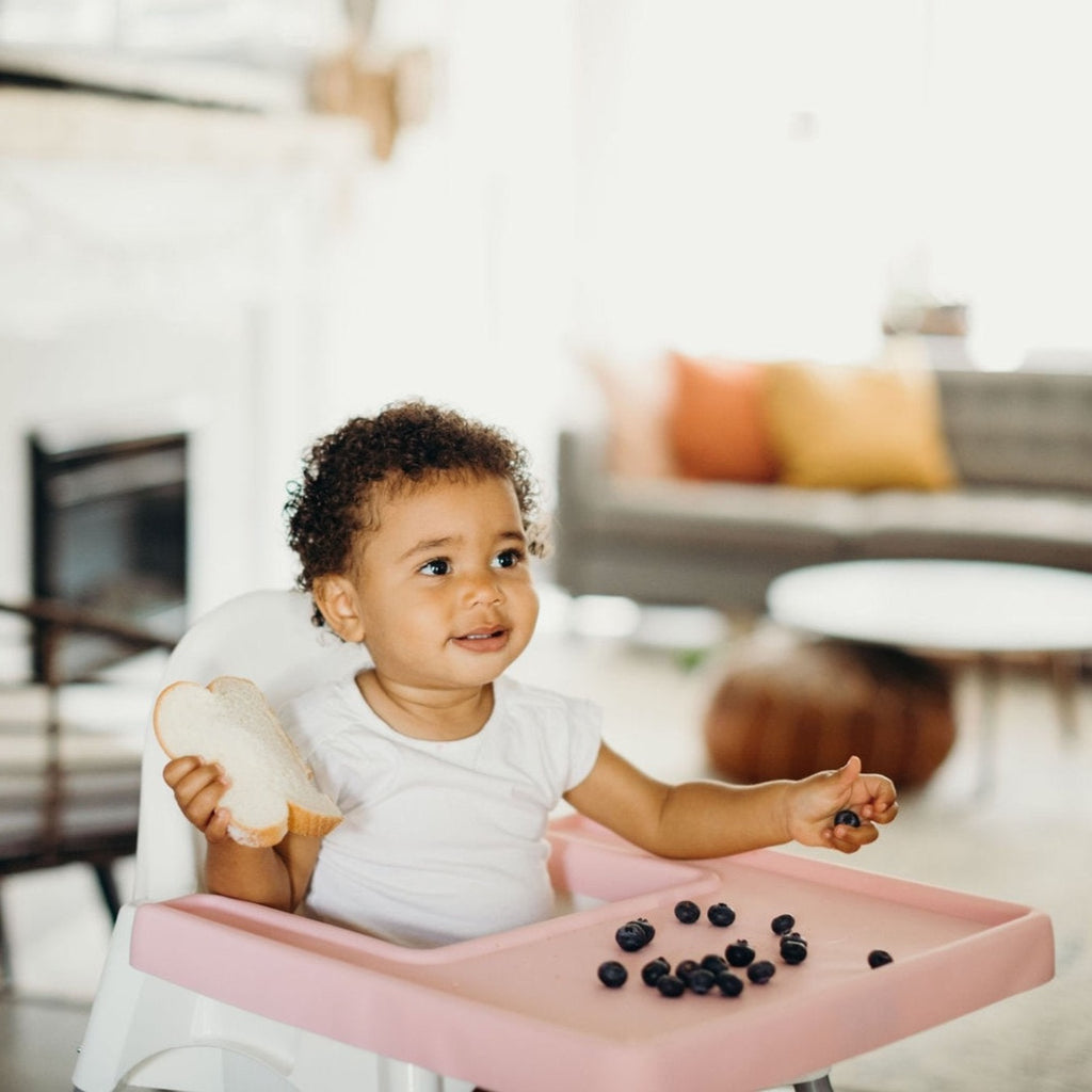 Child in Ikea Antilop Highchair eating Blueberries off of the rosy pink style full coverage placemat cover