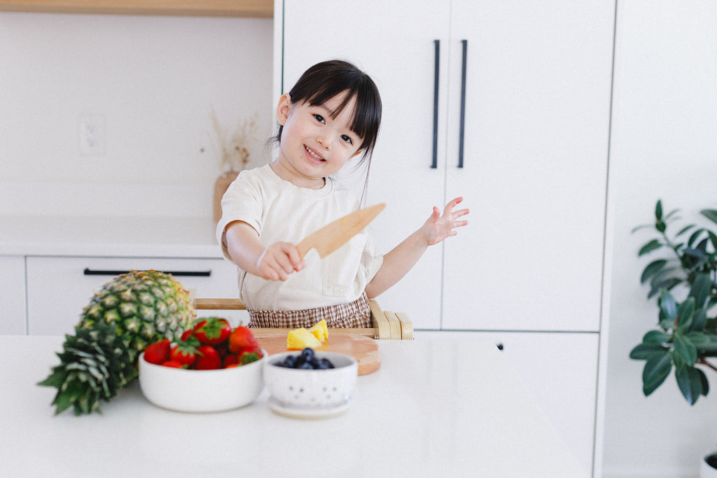 a little girl holding a wooden chopper knife to cut some fruits