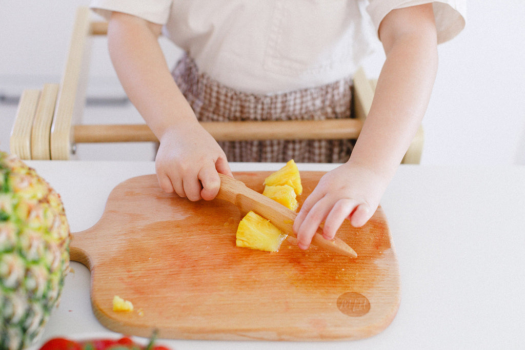 a little girl cutting pineapples with her wooden knife