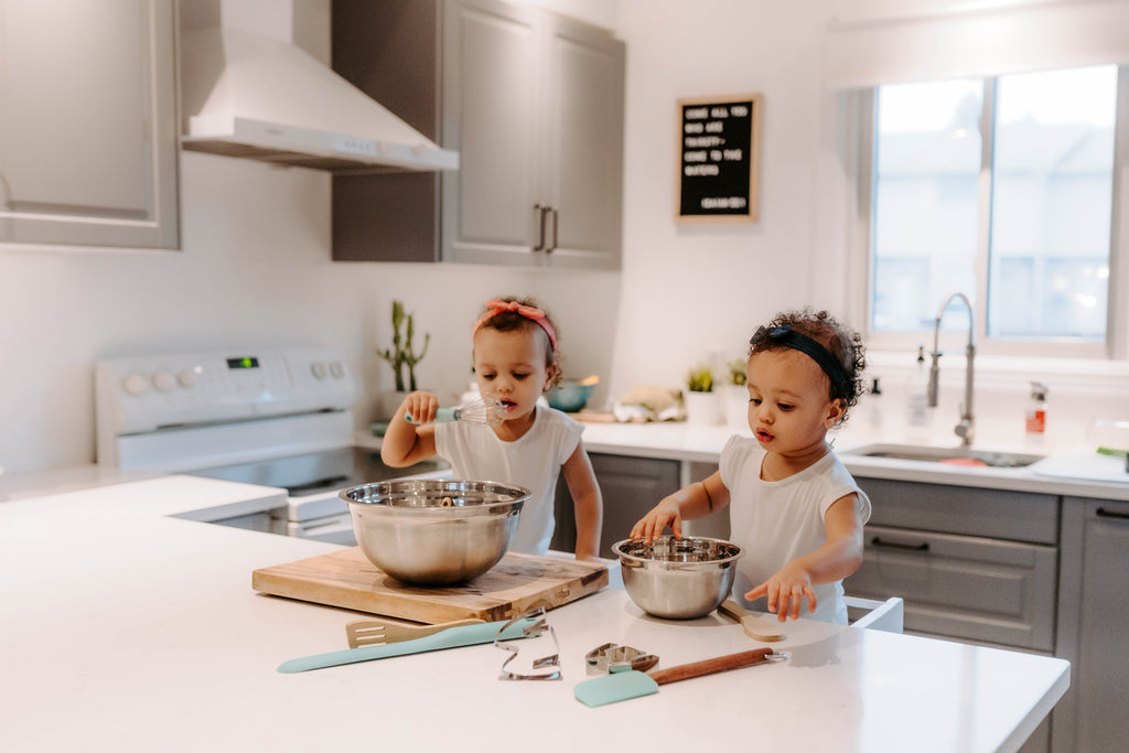 Twin toddler sisters explore mixing and stirring independently in their learning tower kitchen stools. 
