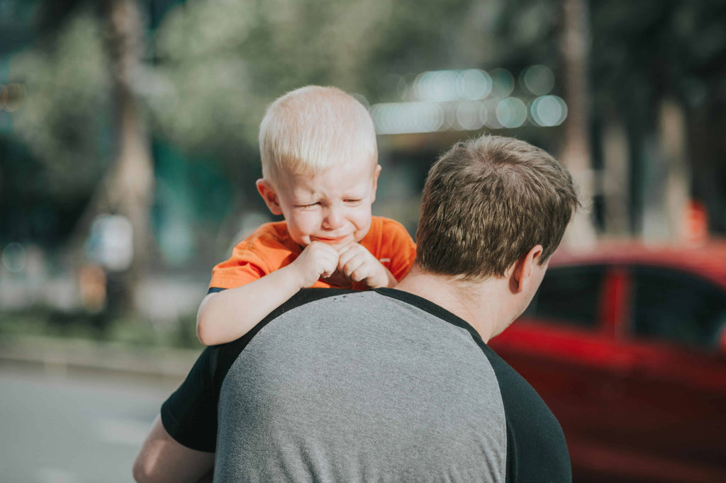 a kid crying while being carried by his dad