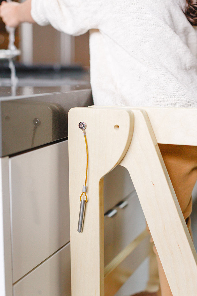 A detail shot of a wooden folding learning tower showing the pin that can be inserted holding the extra safety bar in place. 