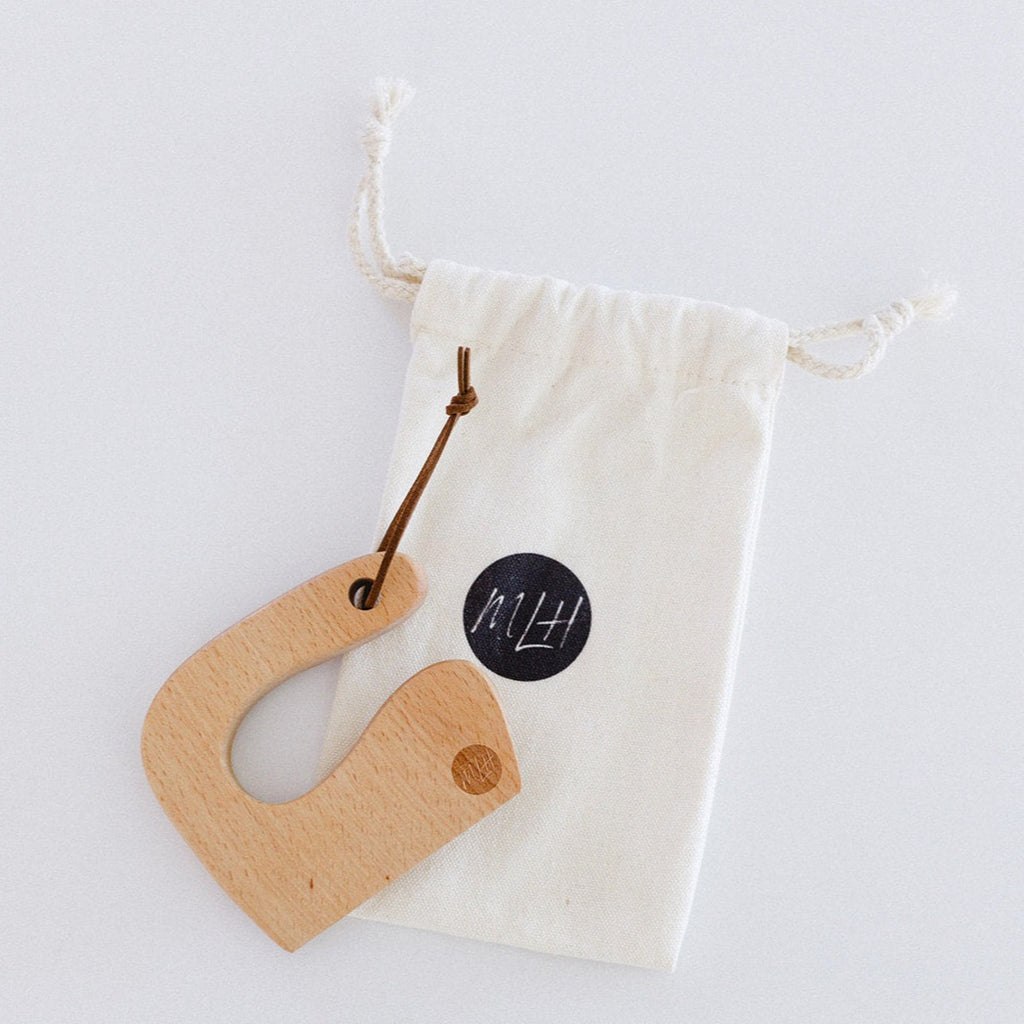 A wooden beginner toddler knife laying flat on a cotton drawstring bag with a white background. 