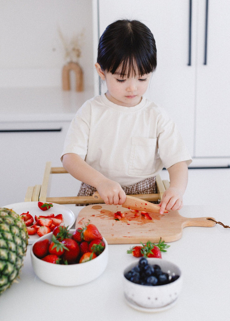 A girl chopping strawberries with her wooden toddler chopper. 