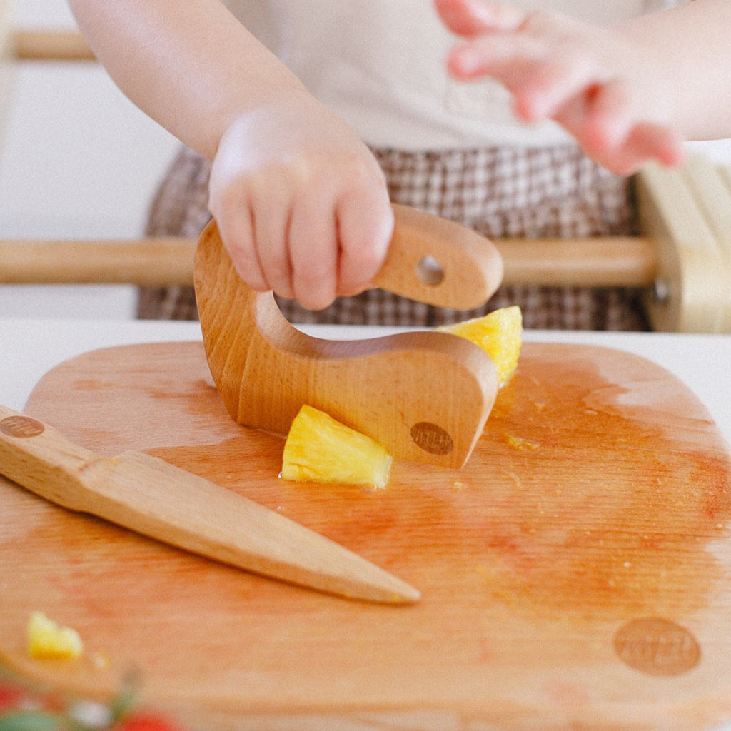 A girl chopping pineapple with her wooden toddler knife. 
