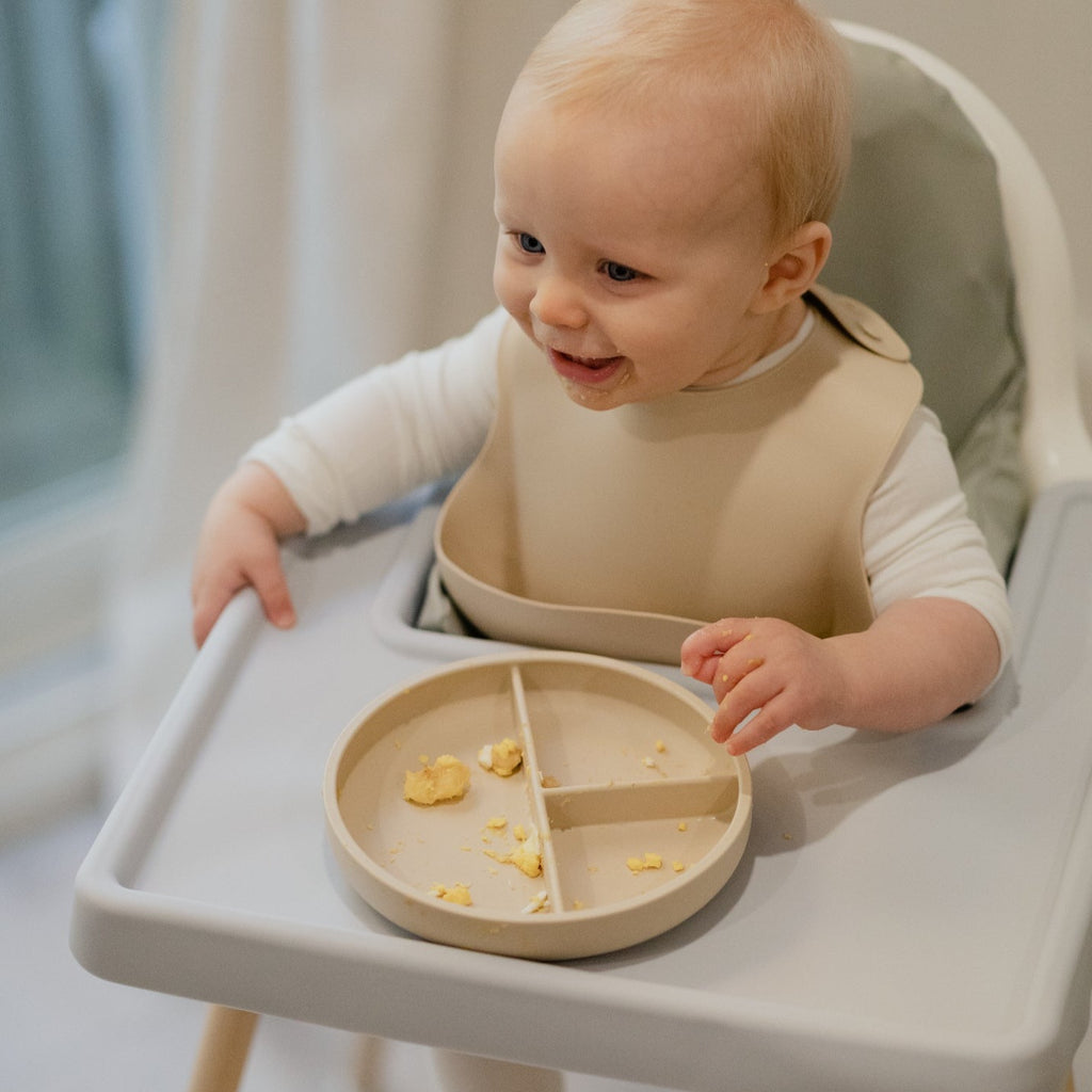 A young boy sitting in highchair with the silicone highchair placemat keeping everything clean. 