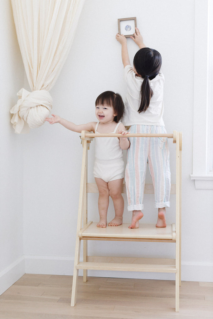 A set of sisters hanging pictures and playing with curtains while in their double wide learning tower. 