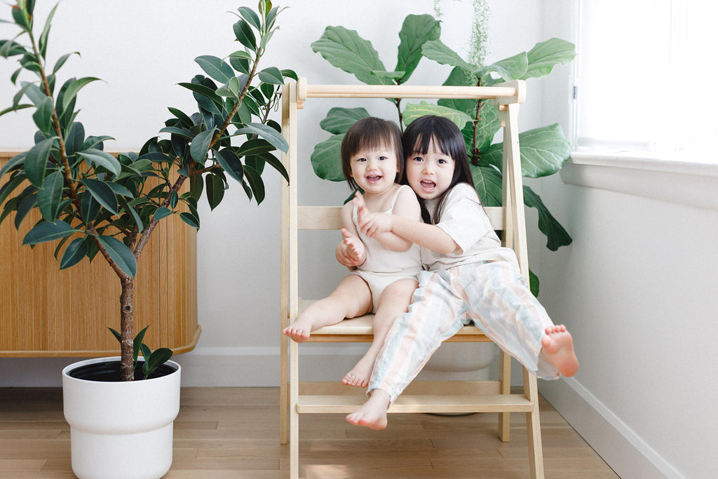 A sister duo clapping hands while sitting in a double wide learning tower. 