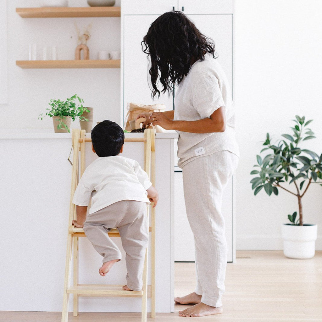 A boy climbing up into his wooden learning tower to help mom plant some seedlings. 