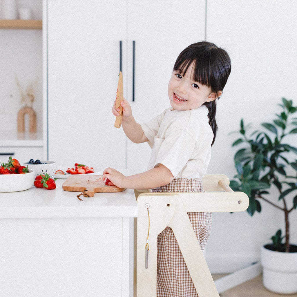 A girl smiling in her learning tower while breaking from chopping strawberries. 