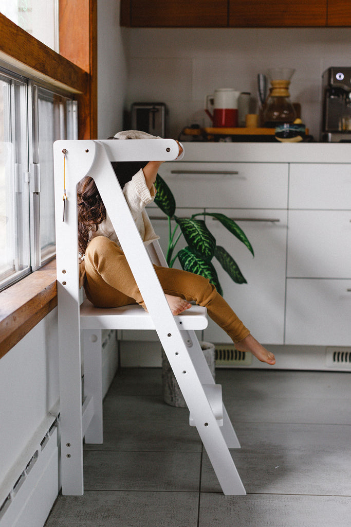 A daughter independently climbing down out of the white foldable learning tower. 