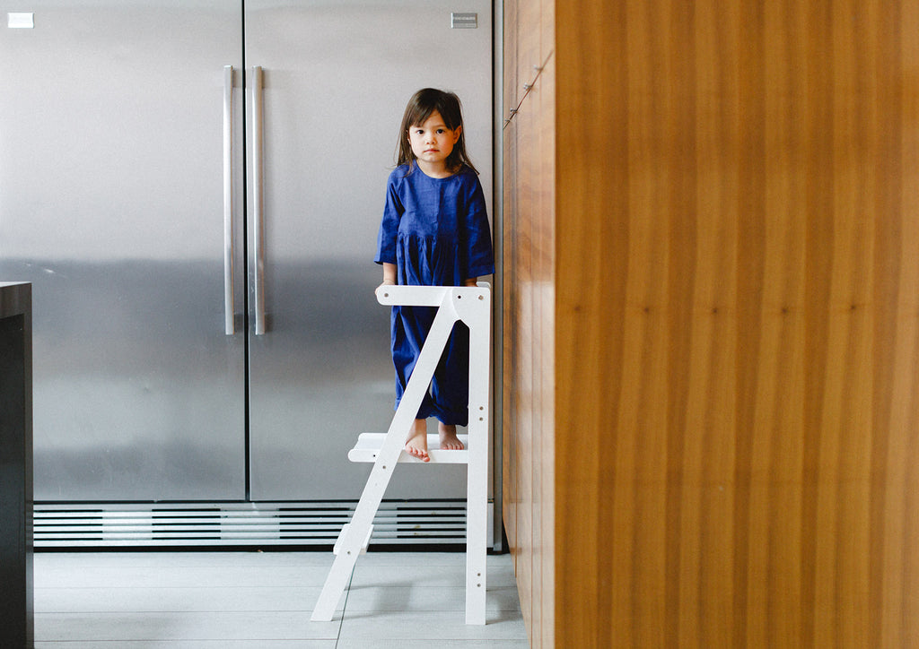 A girl wearing a royal blue dress standing and posed looking at the camera white standing in a white learning tower. 