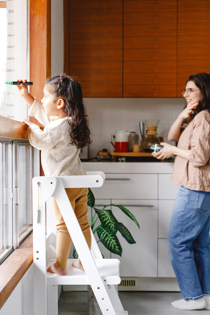 Woman and child in a kitchen with the child on a step stool.