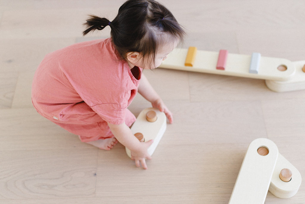 a little girl is holding a piece of the balance beam set