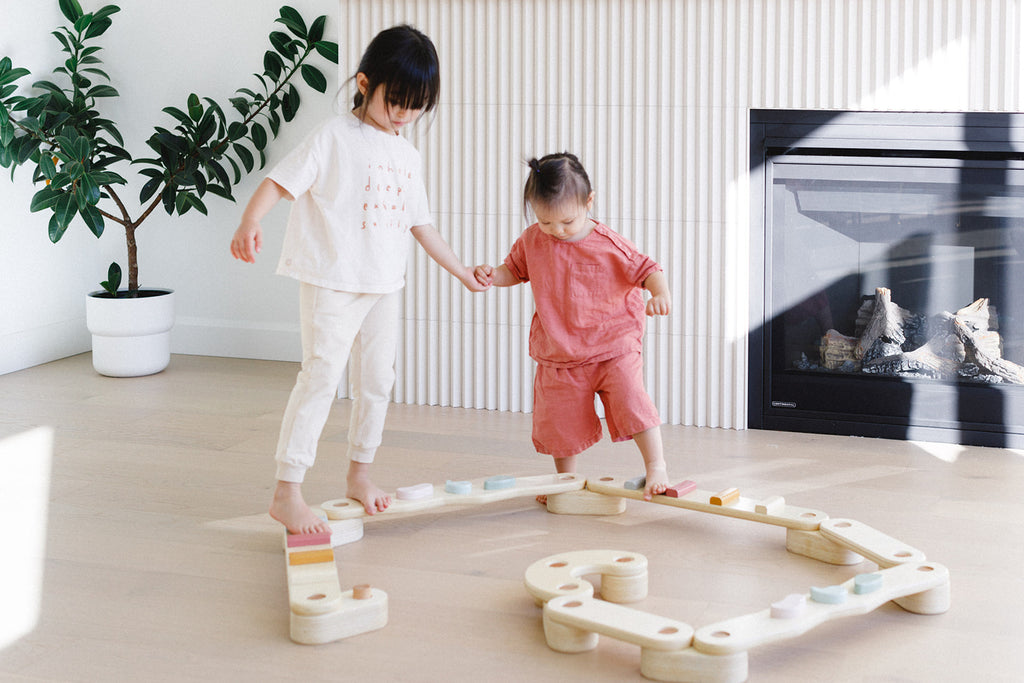 a little girl is helping the other girl to walk on the beam