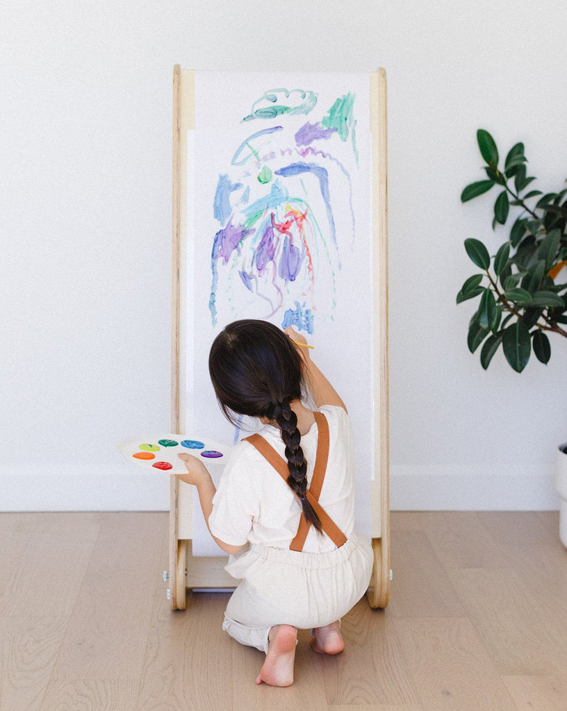 a little girl is painting on the slide easel