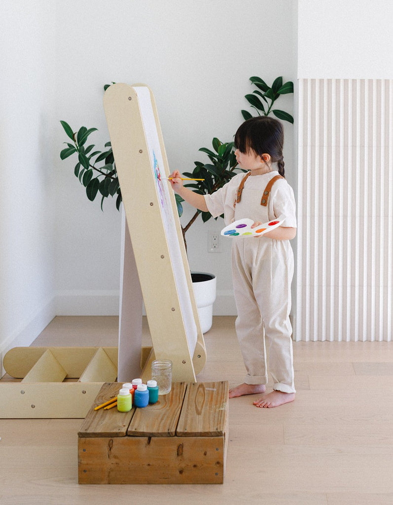 a little girl is painting on her slide easel