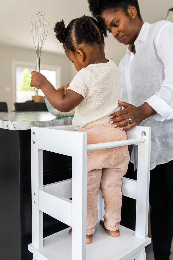 Woman teaching a young child how to use a whisk in a kitchen.