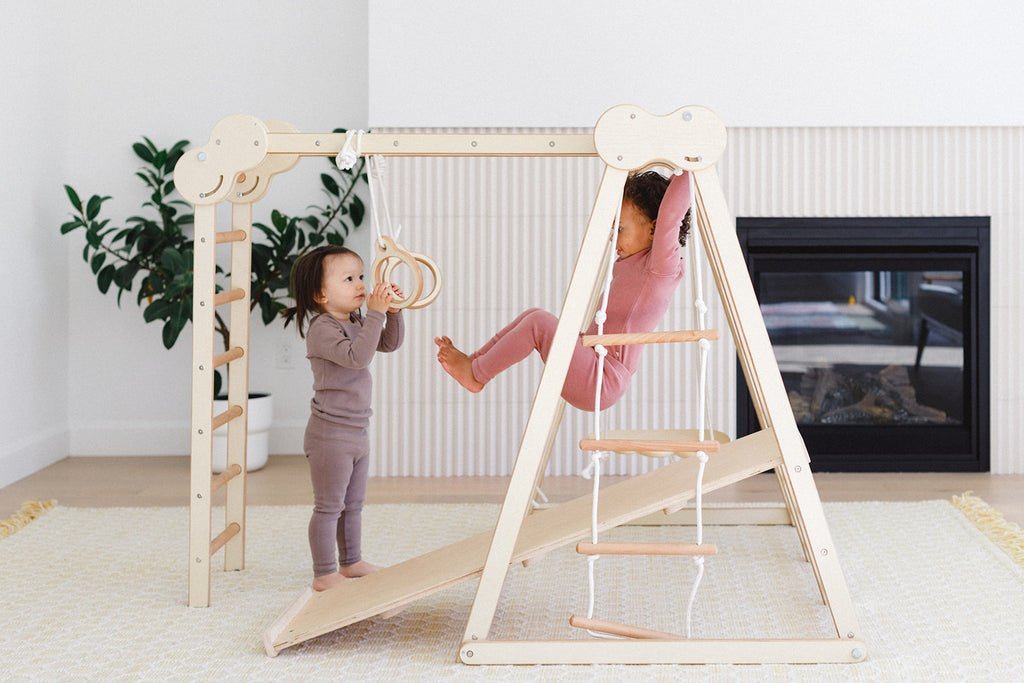 a little girl is holding the ring set while the other one is climbing at the monkey bars