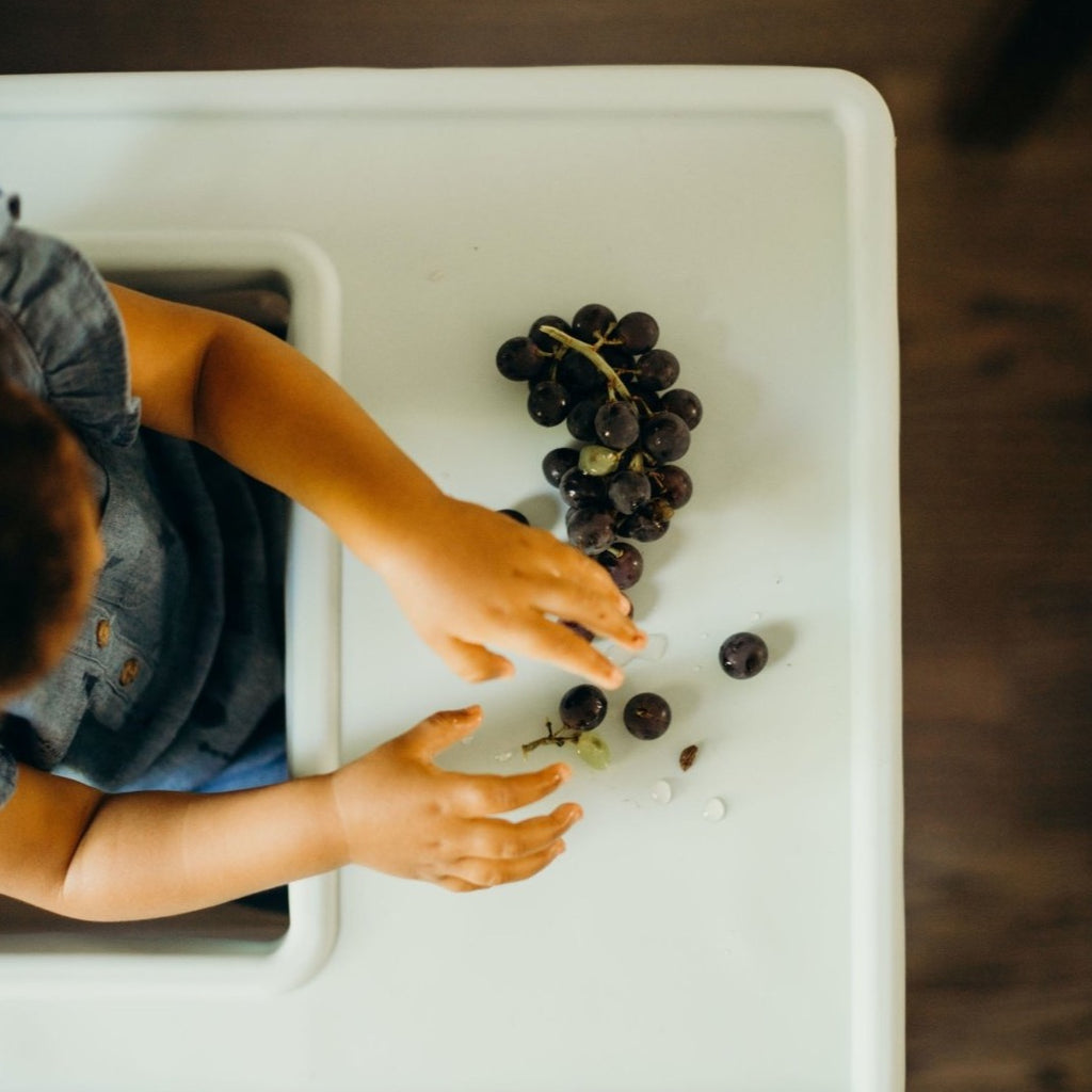 Child in Ikea Antilop Highchair eating Blueberries off of the mint green style full coverage placemat cover