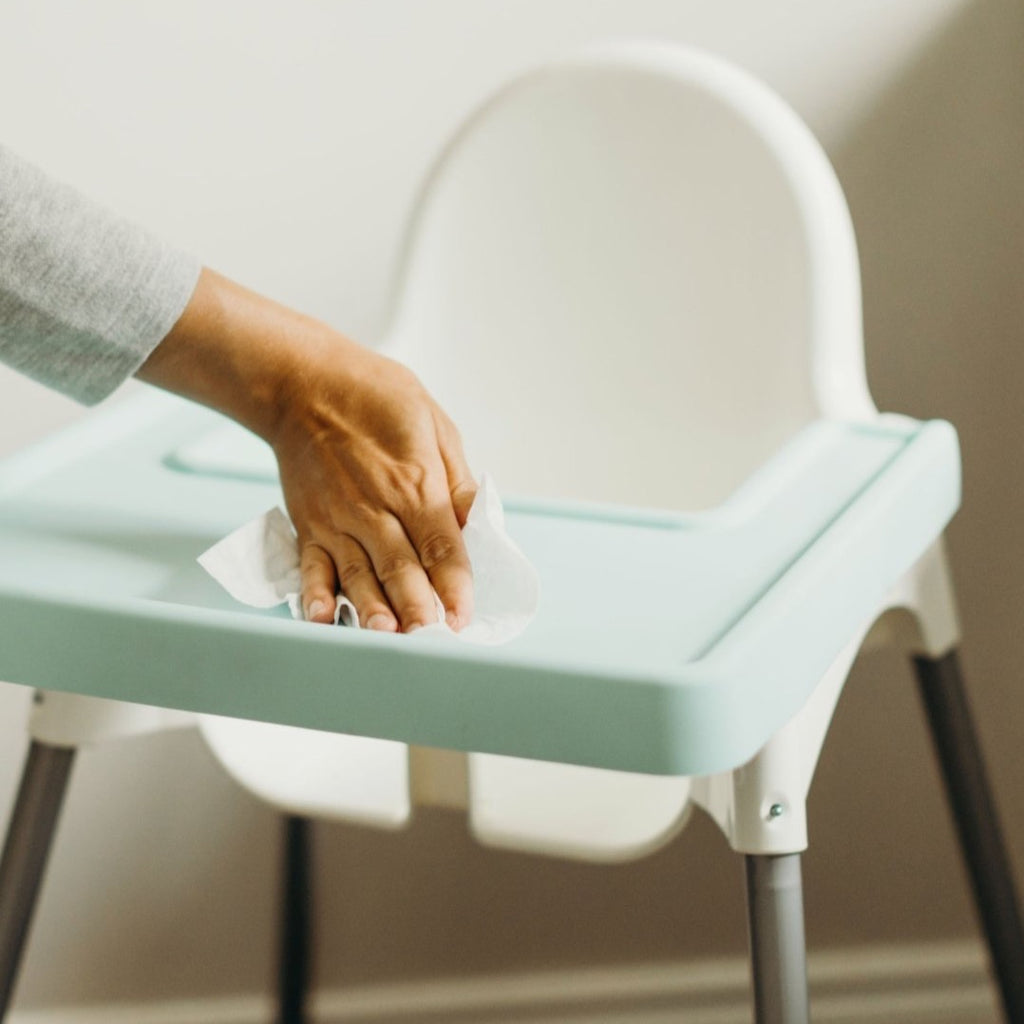 Overhead view of parent wiping down mint green full coverage Ikea Antilop placemat cover easily and safely with a wipe