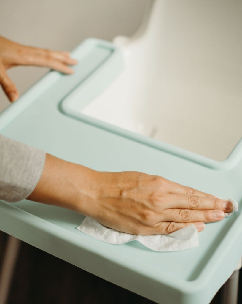 Overhead view of parent wiping down mint green full coverage Ikea Antilop placemat cover easily and safely with a wipe
