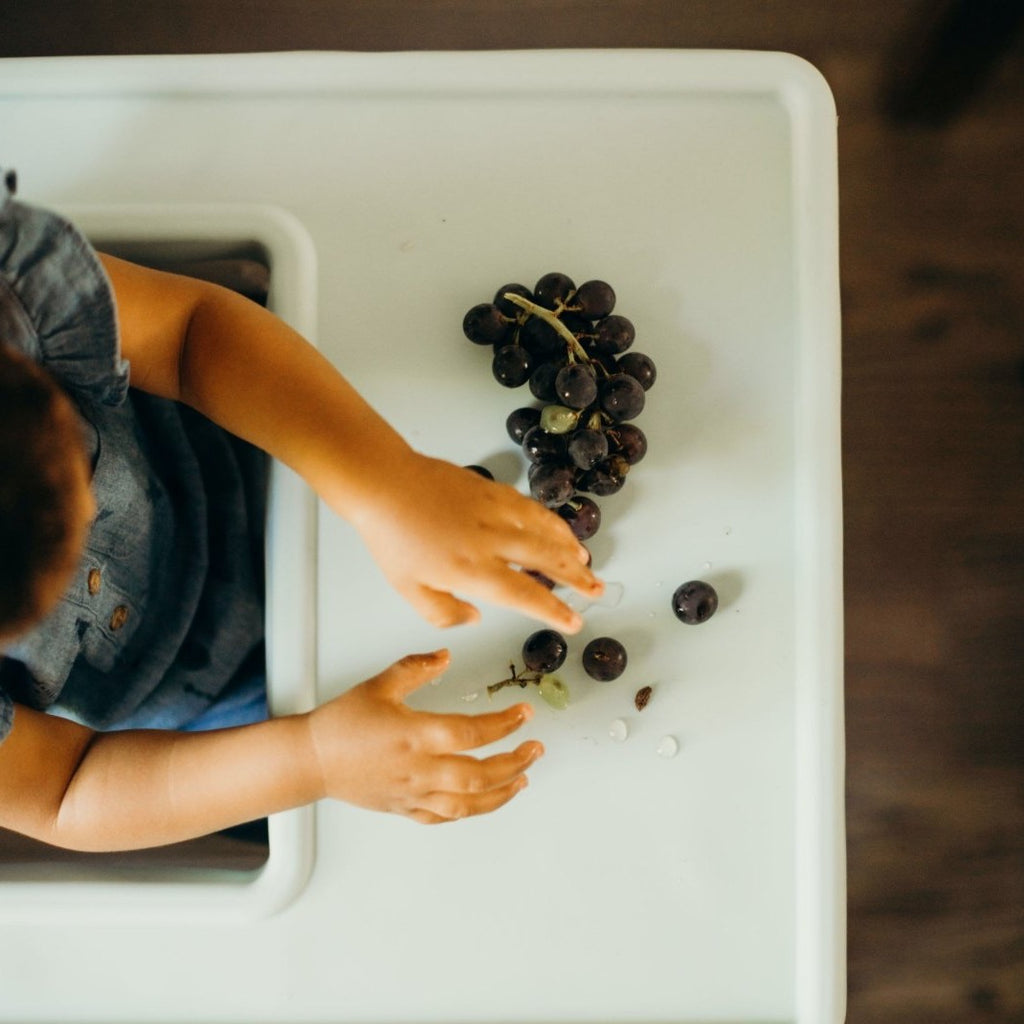Overhead view of a child eating grapes off of the full coverage Ikea Antilop placemat cover
