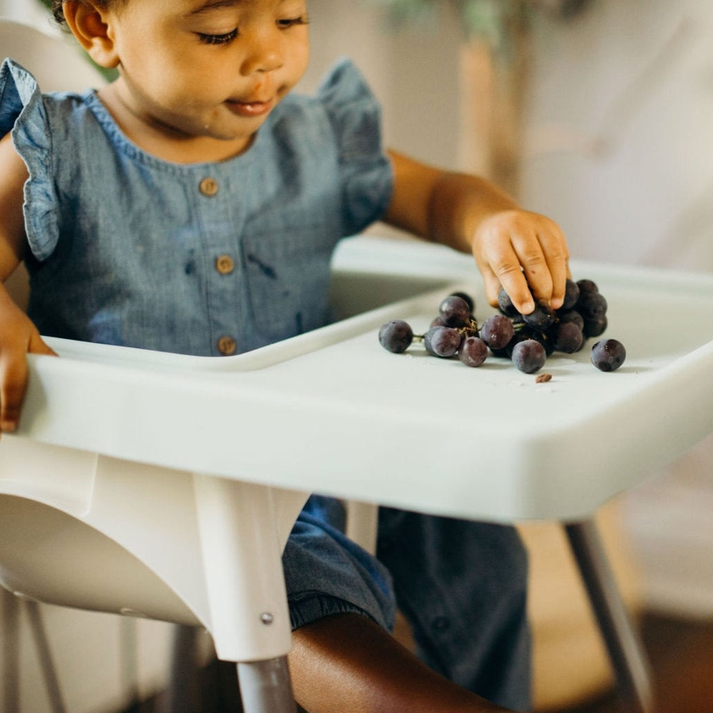 Child in Ikea Antilop Highchair practices baby led weaning by eating grapes off of the mint green style full coverage placemat cover
